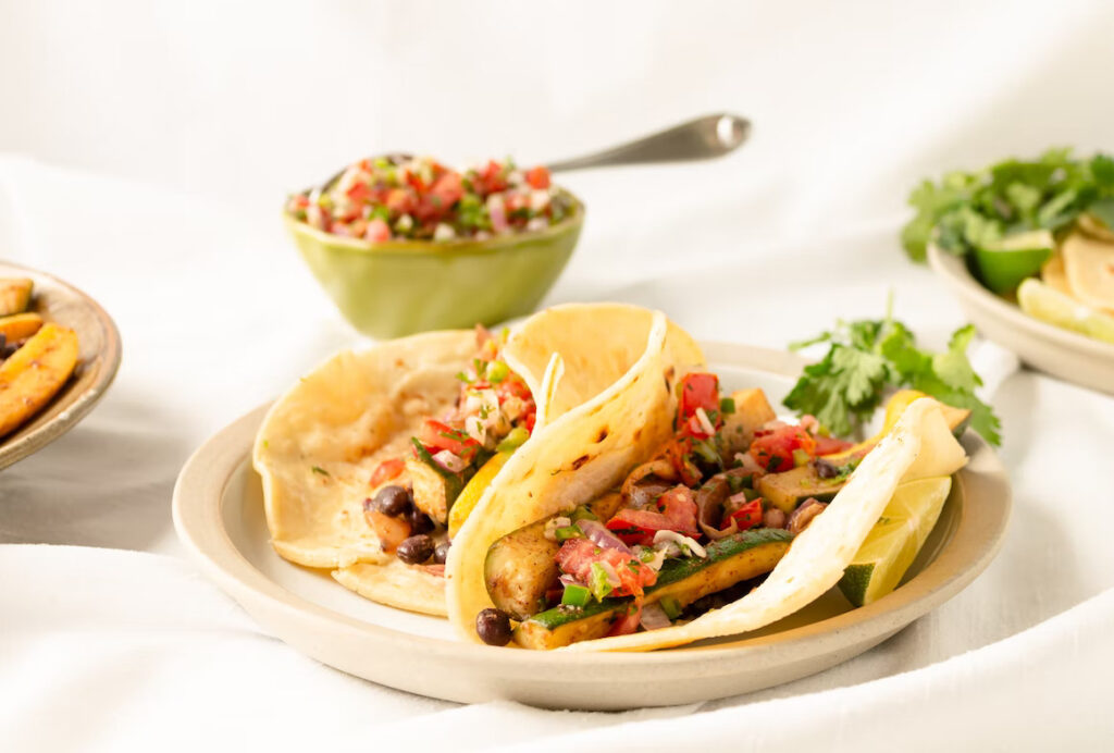 Two tacos on a plate with a blow of salsa in the background