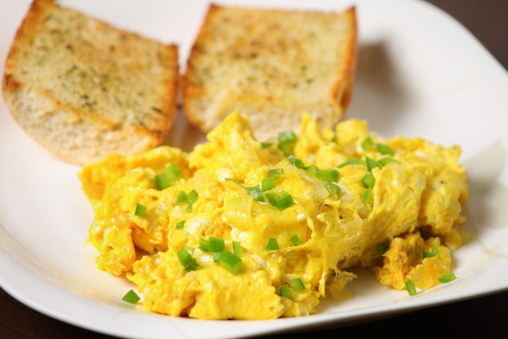 Scrambled eggs on a white plate with a toasted baguette